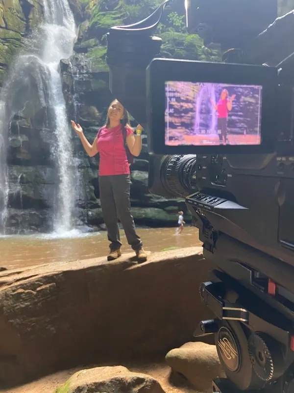 Elaine apresentando diante de uma cachoeira
