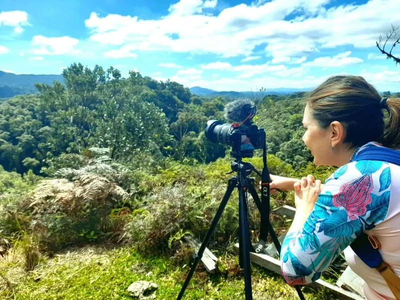 Elaine gravando com câmera no tripé em meio às montanhas